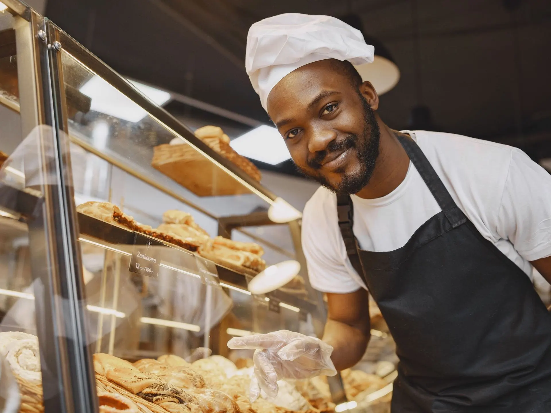Boulanger souriant derrière sa vitrine de pâtisseries